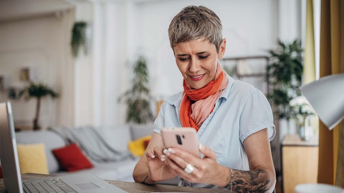 BusinessMobileBanking_ImageBlock_HomeOfficePhone Mature woman sitting at desk at home with phone