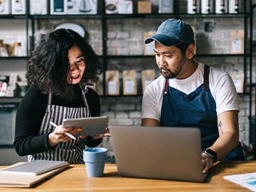 Small business owners working together reviewing information while working with tablet and laptop