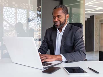 Male banker at work inside office reviewing documents and working on laptop