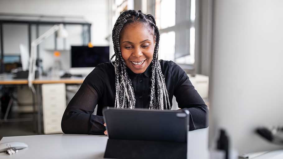 Smiling female executive sitting at her office desk making a video call with digital tablet. African american businesswoman working in office having a video conference.