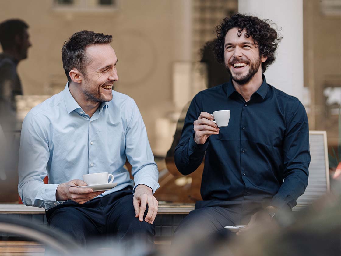 Two coworkers having coffee outside and laughing