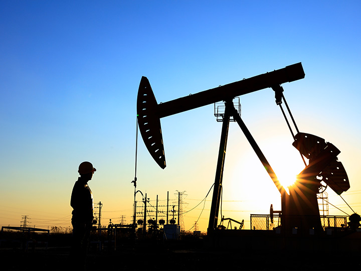 A man looking at pump jack with sunset