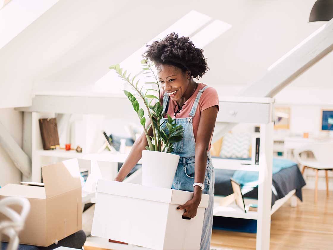 Beautiful African-American young woman carrying her belongings while moving into the new home
