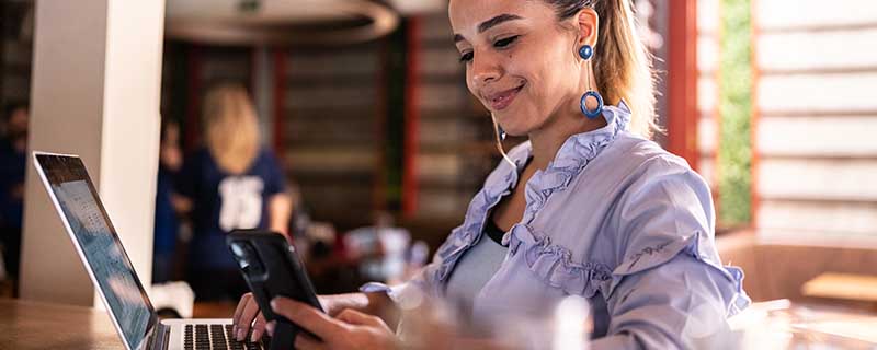 Mid adult woman using the mobile phone and the laptop at her business