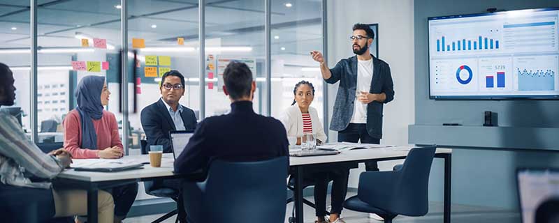 Diverse Modern Office: Businessman Leads Business Meeting with Managers, Talks, uses Presentation TV with Statistics, Infographics. Digital Entrepreneurs Work on e-Commerce Project