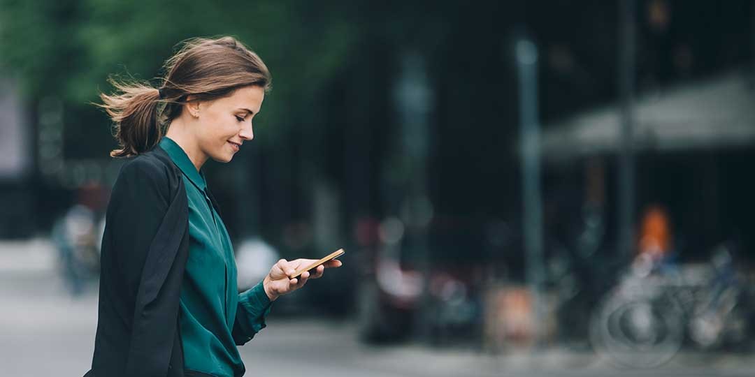 Confident businesswoman using smart phone while crossing street in city