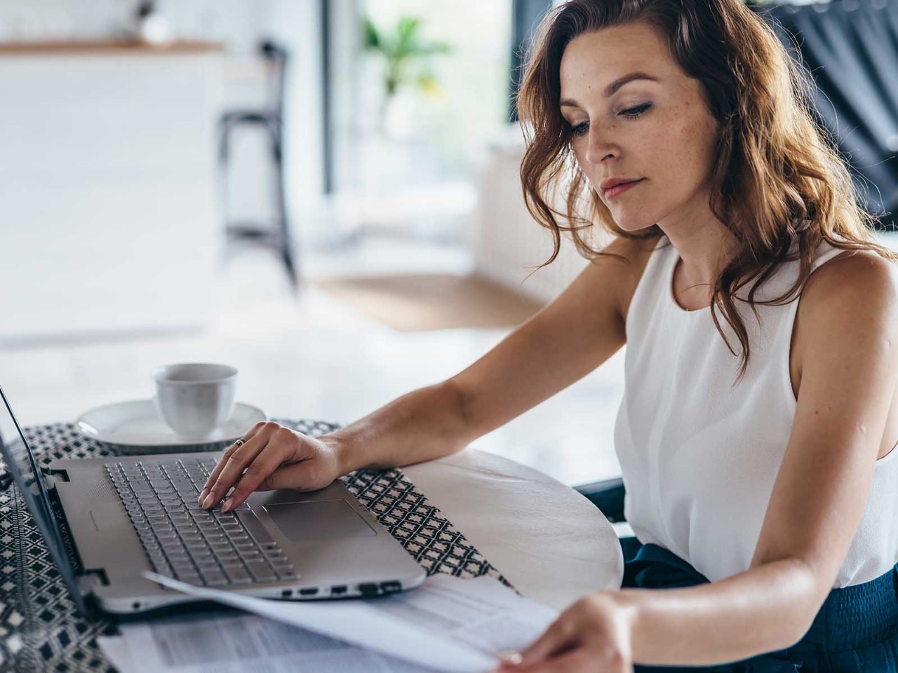 Woman using laptop while sitting at table. Young businesswoman sitting in kitchen and working on laptop