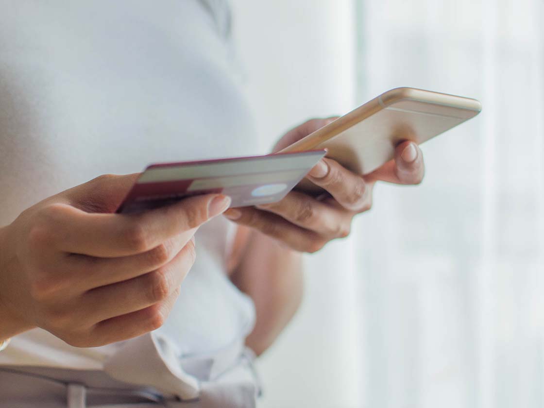 ApplePay_HorizontalFeature_WomanUsingMobileDeviceAndCreditCard Woman using mobile device and credit card