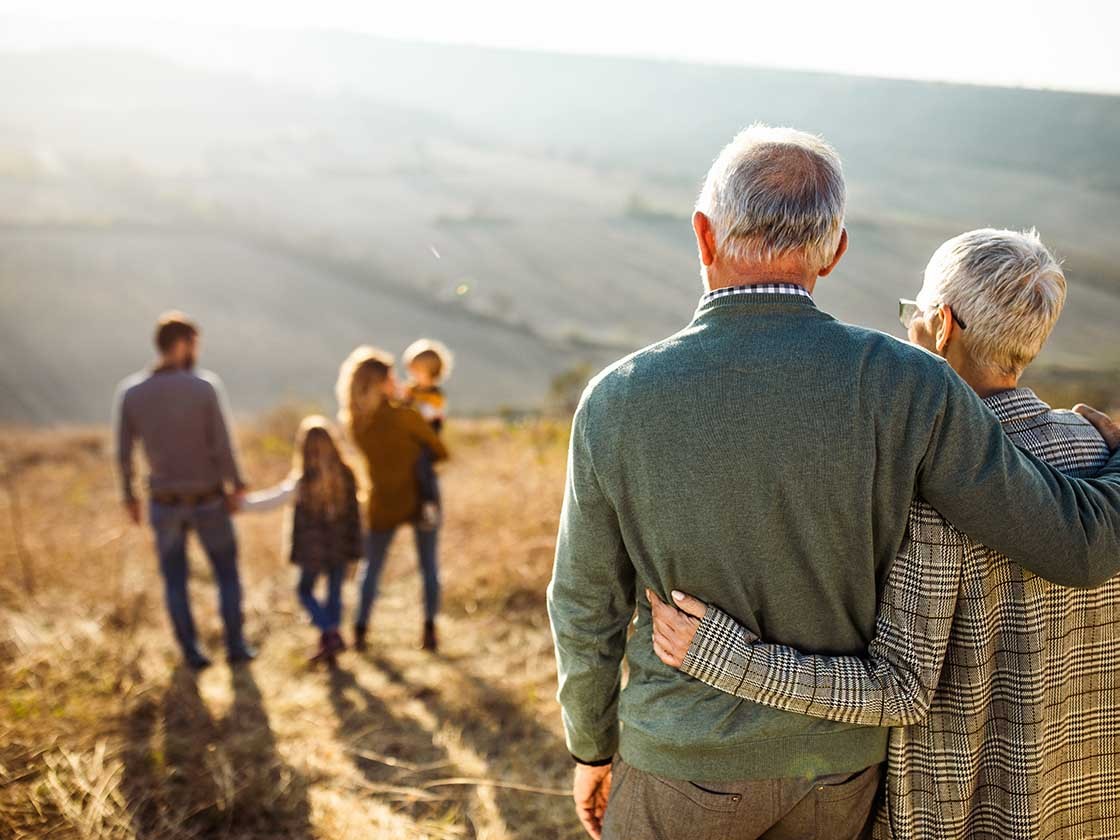 Rear view of embraced senior couple looking at their family in nature